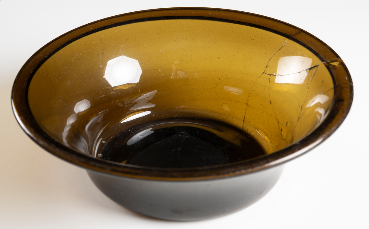 Rund, välvd botten och utsvängd upptill av brunt glas. Lagad.