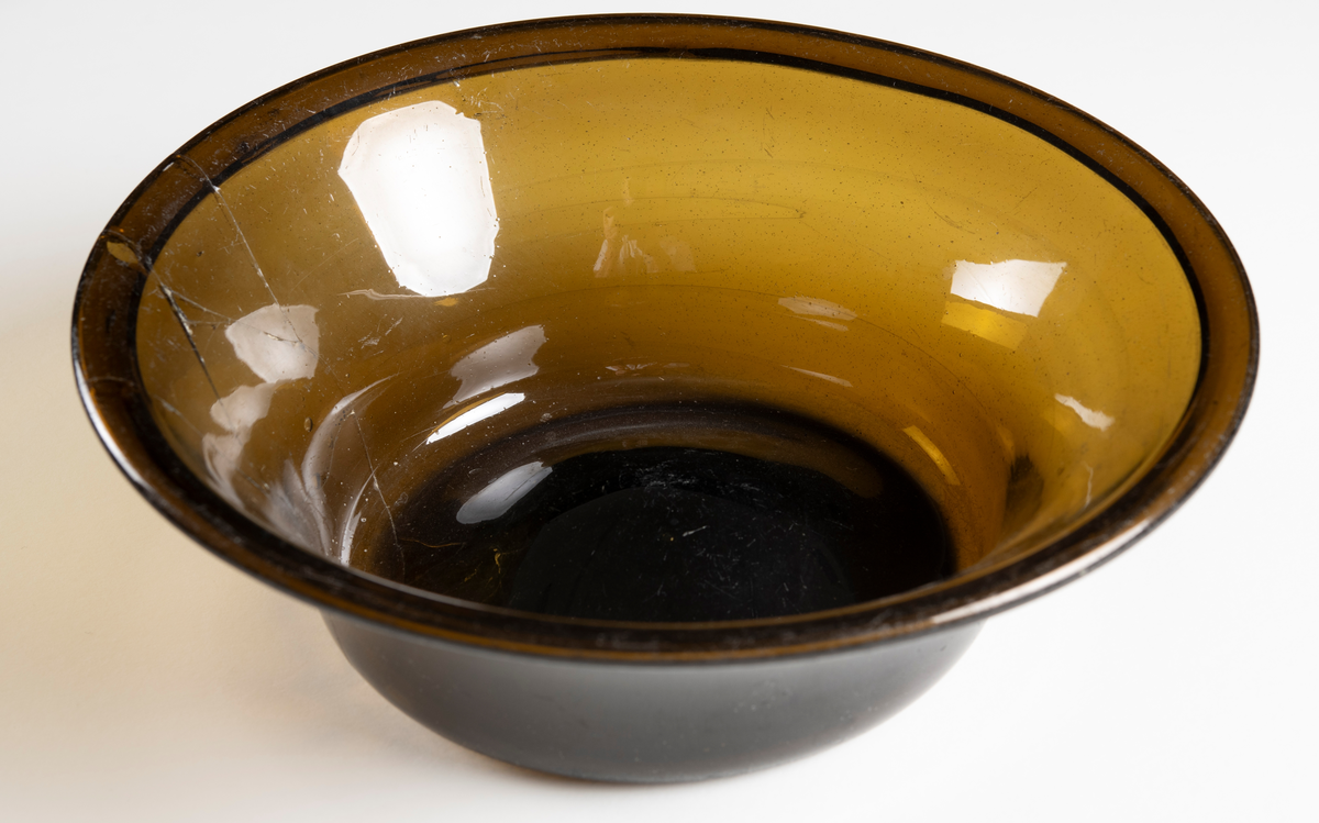 Rund, välvd botten och utsvängd upptill av brunt glas. Lagad.