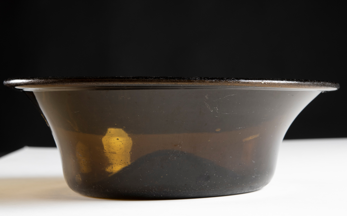 Rund, välvd botten och utsvängd upptill av brunt glas. Lagad.