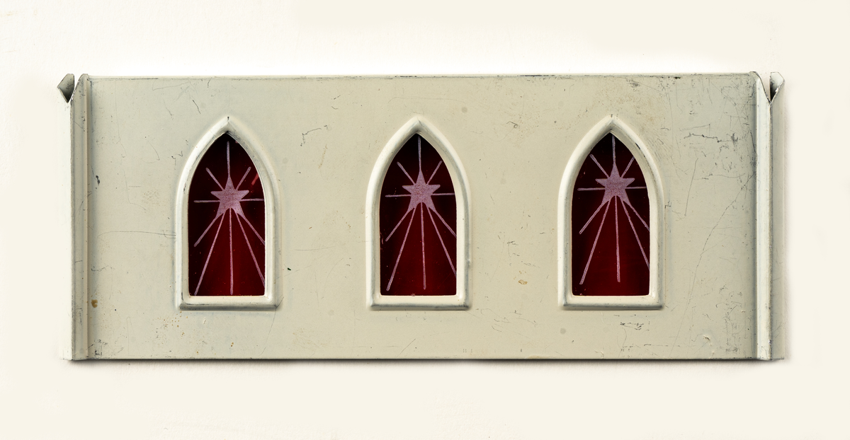 Juldekoration (änglaspel) i form av en kyrka. Vita väggar med grönt tak och spira, röd plast för fönster. Fungerar som ett änglaspel.

Föremålet är omonterat i sin tillhörande pappkartong.