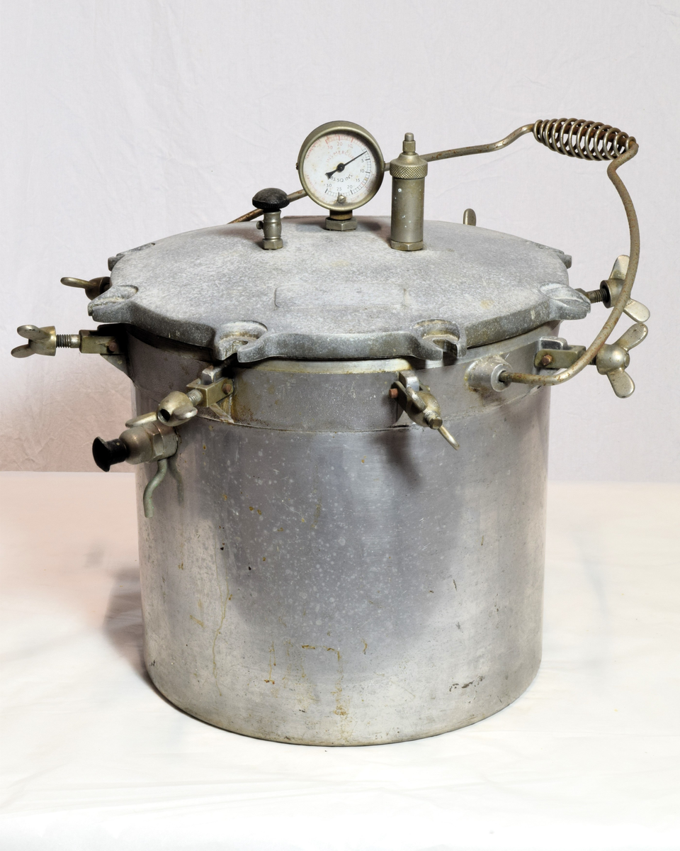 Består av 3 deler: selve aluminiumskjelen med 8 skruhoder, lokk med 8 ører som passer til skruene, trykkmåler samt to ventiler (trykkventiler). Inni en kurv. Lokket melert. Autoklaven ble brukt til sterilisering av legemidler og utstyr som måtte være sterile for produksjon av legemidler.