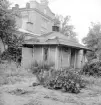 Ett kvarter i förfall. Bild från en serie dokumentationer av bebyggelsen i kvarteret Akilles kort före sanering. Här från det så kallade Stifssekreterarebostället där detta uthus stod mot fängelsemuren. I bakgrunden själva fängelseanläggningen som även den kom att rivas. Foto 1967.