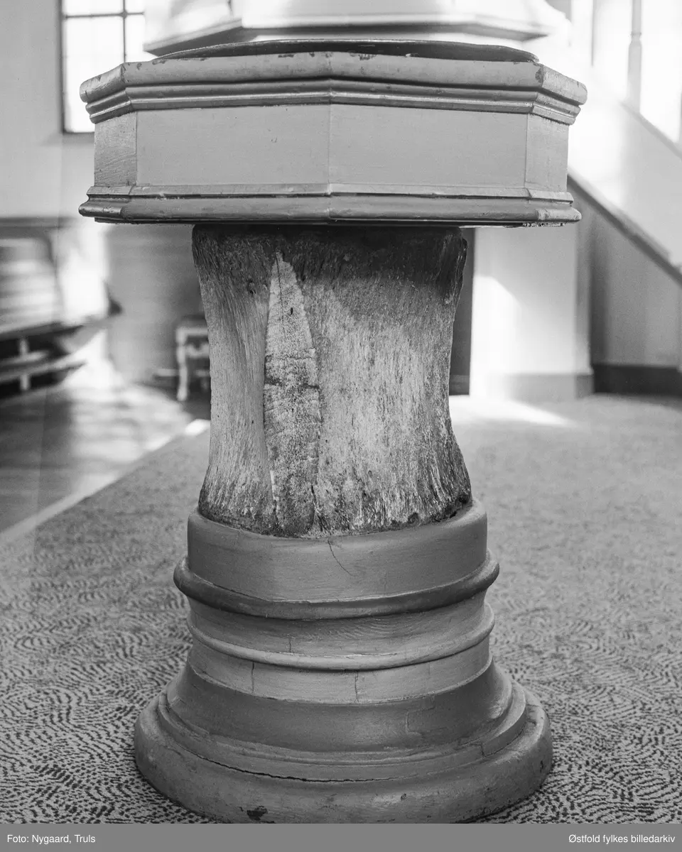 Døpefont i Asak kirke i Halden, fotografert i 1973. Døpefonten i tre har et midtstykke fra bein (ryggvirvel) av en hval. Døpefonten er fra 1700-tallet.