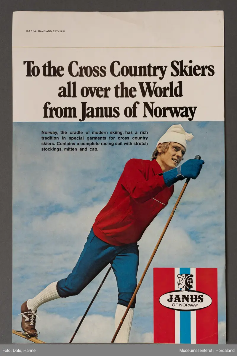 Mann som går på ski i blå, kvite og raude klede, under teksten "To the Cross Country Skiers all over the World from Janus of Norway"