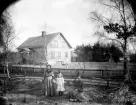 Två kvinnor och ett barn framför bostadshus på okänd plats i Kronobergs län, ca 1900-1910.