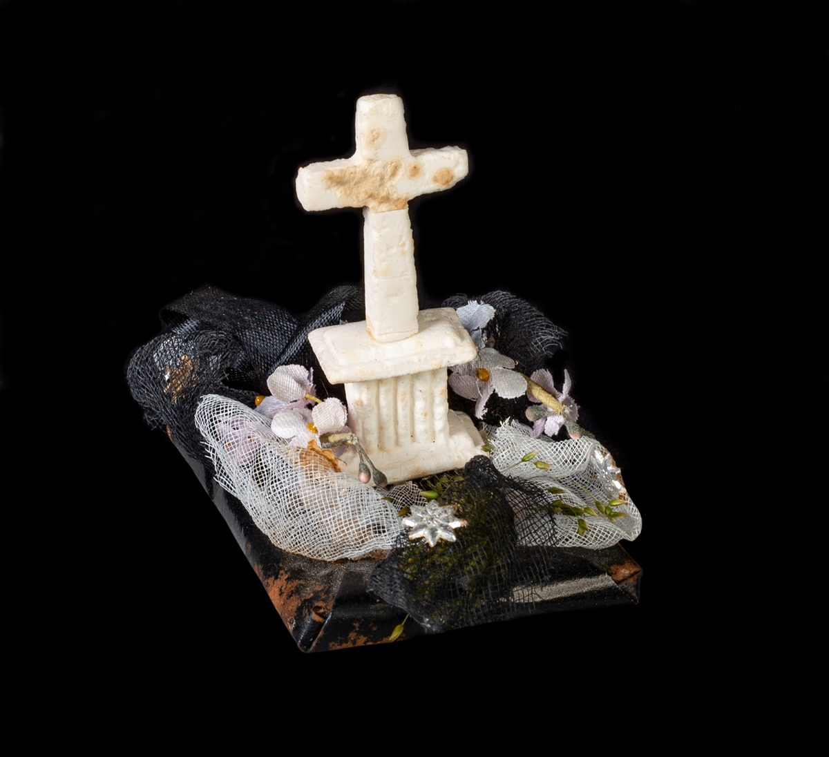 Begravningskaramell med svart tygrosett, pappersgräs, violetta blommor samt vitt, stående kors på svart platta. Korset förmodligen av sockermassa (morsell).
Pappersremsa med text undertill: "Säll är den som slutat har sin strid. Segerkronan fått och evig frid."