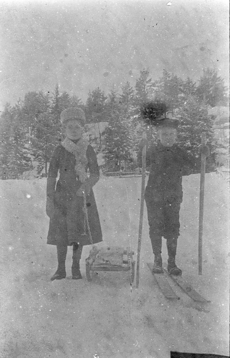 Helga og Per Aasland i vinterklær. Han med ski og hun med kjelke. På Skorta, ca. 1910.