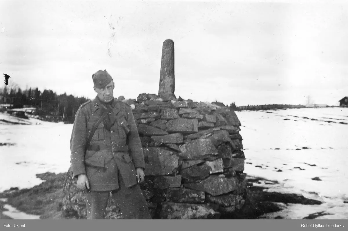 Tekst under bildet: "Fra røiset ved Svenske Moen 1943."  Ukjent person i uniform foran riksgrenserøys mellom Norge og Sverige.
Uvisst hvilken, kanskje nr. 47 Trosterud-grenda i Rømskog?