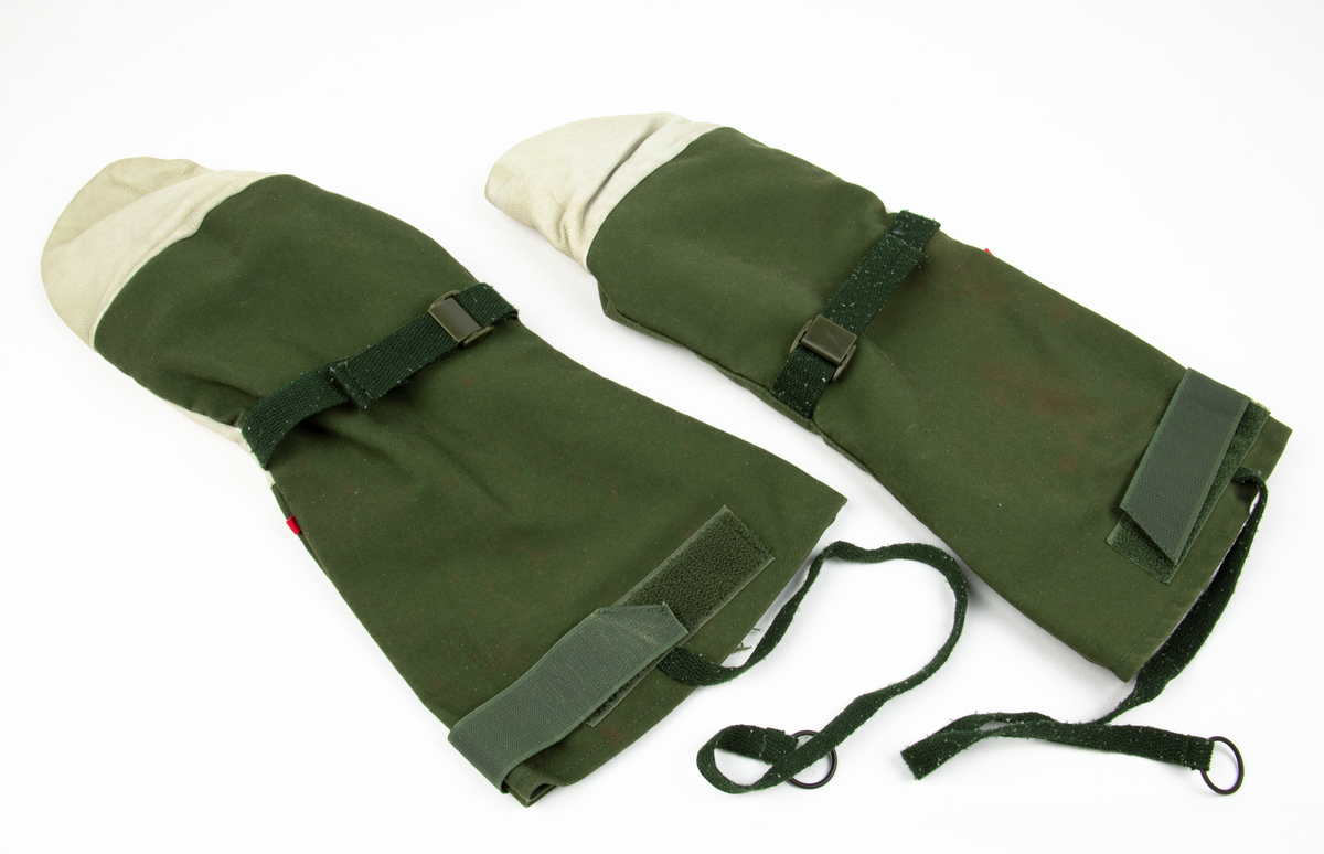 Ett par tumhandskar, fältuniformsystemet 90. Ytterhandsken är förstärkt med vitt gerskin. På handsken sitter remmar samt kardborreband för åtspänning samt remmar med metalring för fastsättning i plagg. I handsken urtagbara fodervantar.