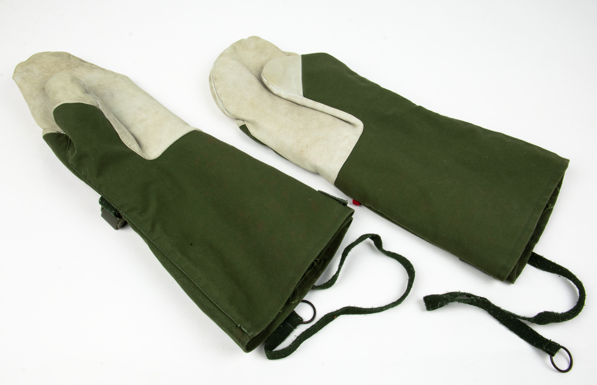 Ett par tumhandskar, fältuniformsystemet 90. Ytterhandsken är förstärkt med vitt gerskin. På handsken sitter remmar samt kardborreband för åtspänning samt remmar med metalring för fastsättning i plagg. I handsken urtagbara fodervantar.