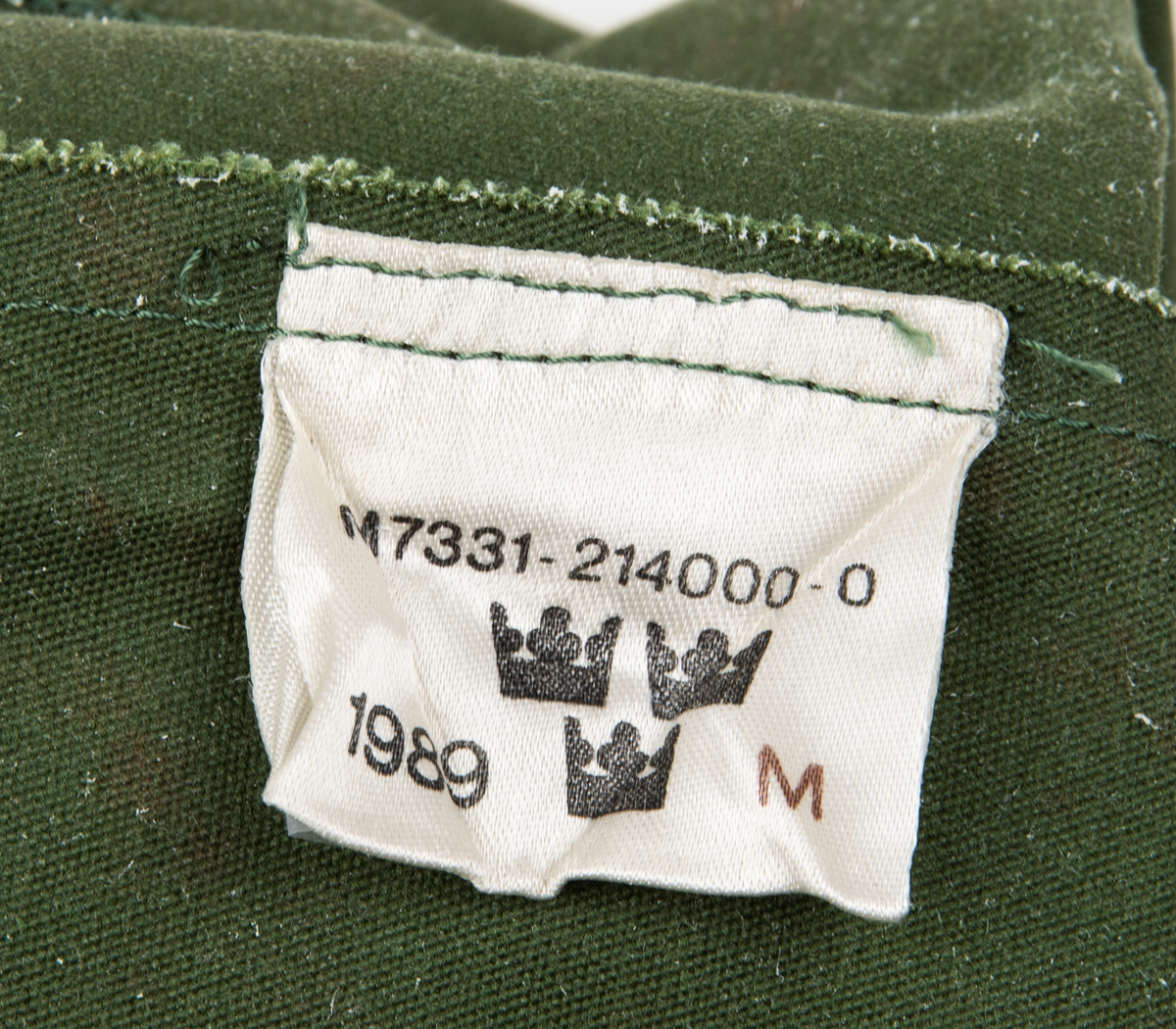 Ett par tumhandskar, fältuniformsystemet 90. Ytterhandsken är förstärkt med vitt gerskin. På handsken sitter remmar samt kardborreband för åtspänning samt remmar med metalring för fastsättning i plagg. I handsken urtagbara fodervantar.
