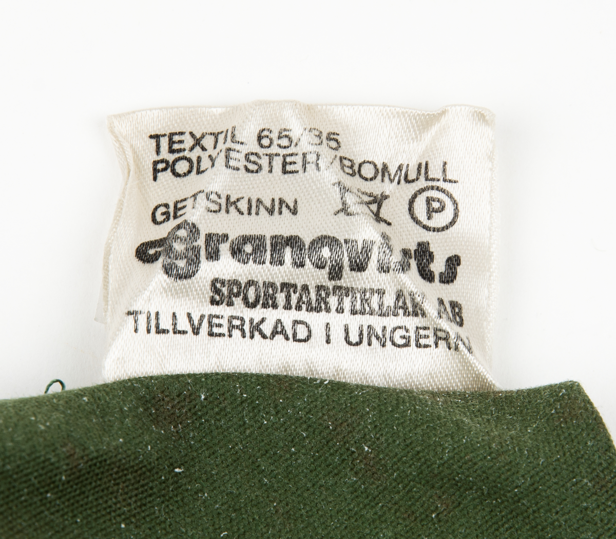 Ett par tumhandskar, fältuniformsystemet 90. Ytterhandsken är förstärkt med vitt gerskin. På handsken sitter remmar samt kardborreband för åtspänning samt remmar med metalring för fastsättning i plagg. I handsken urtagbara fodervantar.