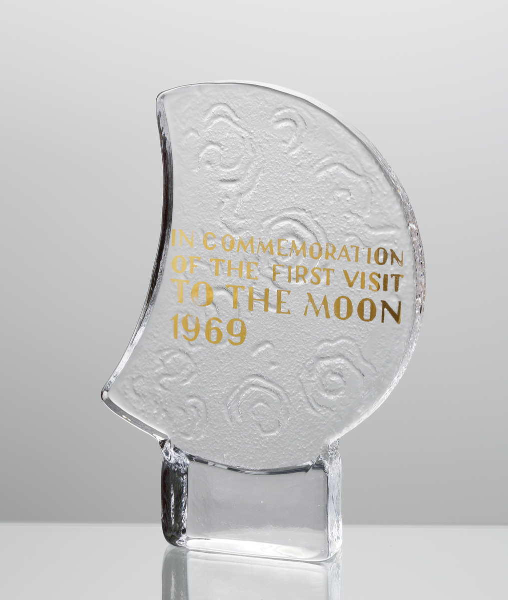 Glasskulptur föreställande en halvmåne. Text i guld "IN COMMEMORATION OF THE FIRST VISIT TO THE MOON 1969". Formgiven av Christer Sjögren. Tillverkad i samband med den första månlandningen 1969. Lindshammar glasbruk skickade ett antal examplar runt om i världen, bla a till Nordiska museet, Nationalmuseum, Utvandrarnas hus i Växjö, svenske kungen och vita huset. I arkivet finns några tackbrev från tacksamma mottagare, bland annat Richard Milhouse Nixon. Nixons tackbrev finns bifogat i denna post.
Inskrivet i huvudkatalogen tidigast 1969.