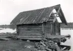 Fiskebod. Längd mellan gavlarnas yttersidor 3,17 meter. Bredd mellan väggarnas ytterliv 3,43 meter. Svale vid båda gavlarna. Vertikala dubbelhaksknutar. Foto från sydväst.