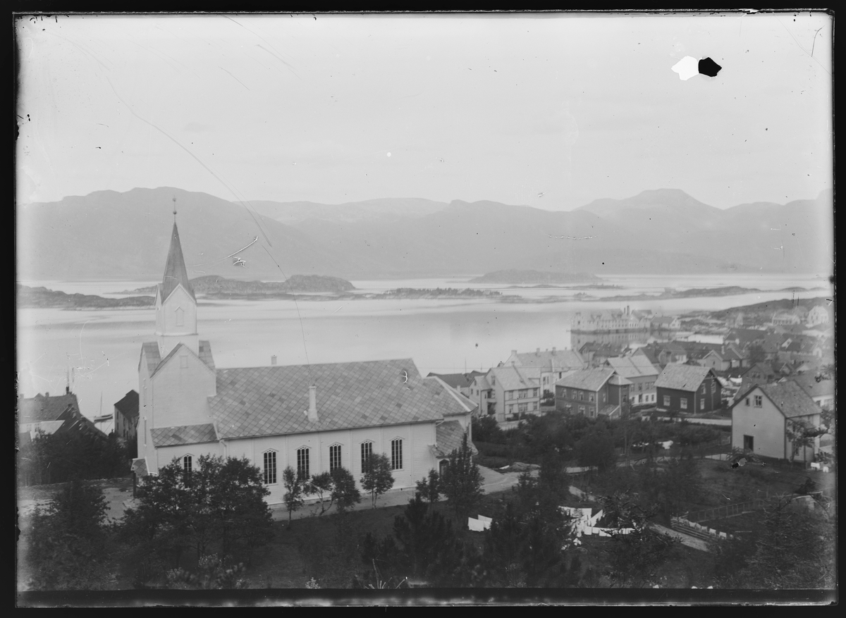Utsikt over Florø med den hvite kirken i forgrunnen. Foran og til høyre for kirken står det tett med trehus. I bakgrunnen, ute i vannet er det rader av holmer og lave fjell.