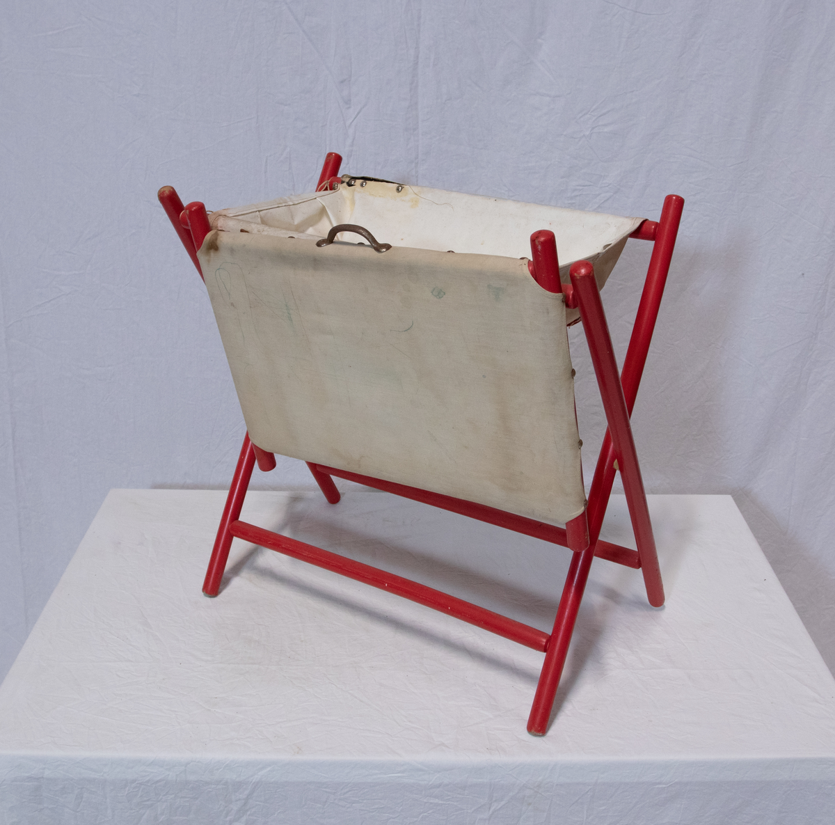 Stellebord til dukke. Rødmalt trekonstruksjon av runde pinner, tappet sammen i kryss i bena. Kan slås sammen. Badekar naglet fast i trerammen, laget av plast/vinyl. Badekaret har propp med slange i bunnen. Stellematte kan legges oppå badekaret, denne er laget i bomull. Stellematte stives av ved to lærstropper under, disse er spikret fast. Påfestet bærhåndtak i toppen av metall, skrudd med to skruer. På ene siden ett stykke med lysblå plast med tre lommer, hele stykket og lommene er kantet med rødrutete stoff.