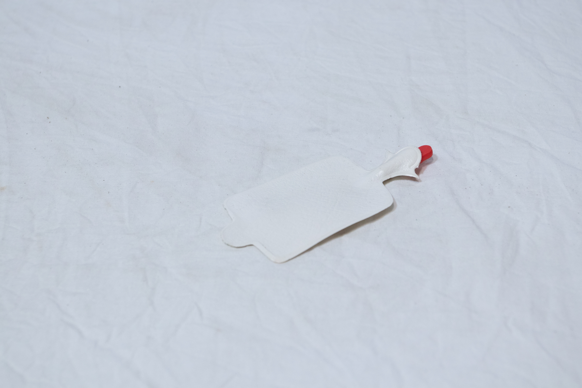 Stellebord til dukke. Rødmalt trekonstruksjon av runde pinner, tappet sammen i kryss i bena. Kan slås sammen. Badekar naglet fast i trerammen, laget av plast/vinyl. Badekaret har propp med slange i bunnen. Stellematte kan legges oppå badekaret, denne er laget i bomull. Stellematte stives av ved to lærstropper under, disse er spikret fast. Påfestet bærhåndtak i toppen av metall, skrudd med to skruer. På ene siden ett stykke med lysblå plast med tre lommer, hele stykket og lommene er kantet med rødrutete stoff.