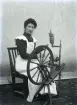Fie Anna Karlsson, Fäi-Jakås dotter, 18 år, spinner lin. Hon är fint uppklädd och spinner inomhus.