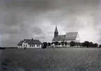 Söder om kyrkan var förr bara åkrar, så när som på en liten markplätt avsatt för sockenmagasinet mitt emot kyrkans södra stiglucka. 1897 flyttade man sockenmagasinet till öster om kyrkan där förut skolan låg och byggde en ny modern skola framför kyrkan.

Vid skolans synliga gavel och tre fönster in på långsidan låg den s k storskolan och vid andra gaveln med två fönster på långsidan låg småskolan. I vinkelbygget var det lärarbostäder. Skolan är således endast 5 år gammal på bilden. Någon väg till Sunnkörke och Gannor gick inte förbi skolan vid denna tid. En östlig väg gick från kurvan vid Lau f d kvarn och en västlig, 