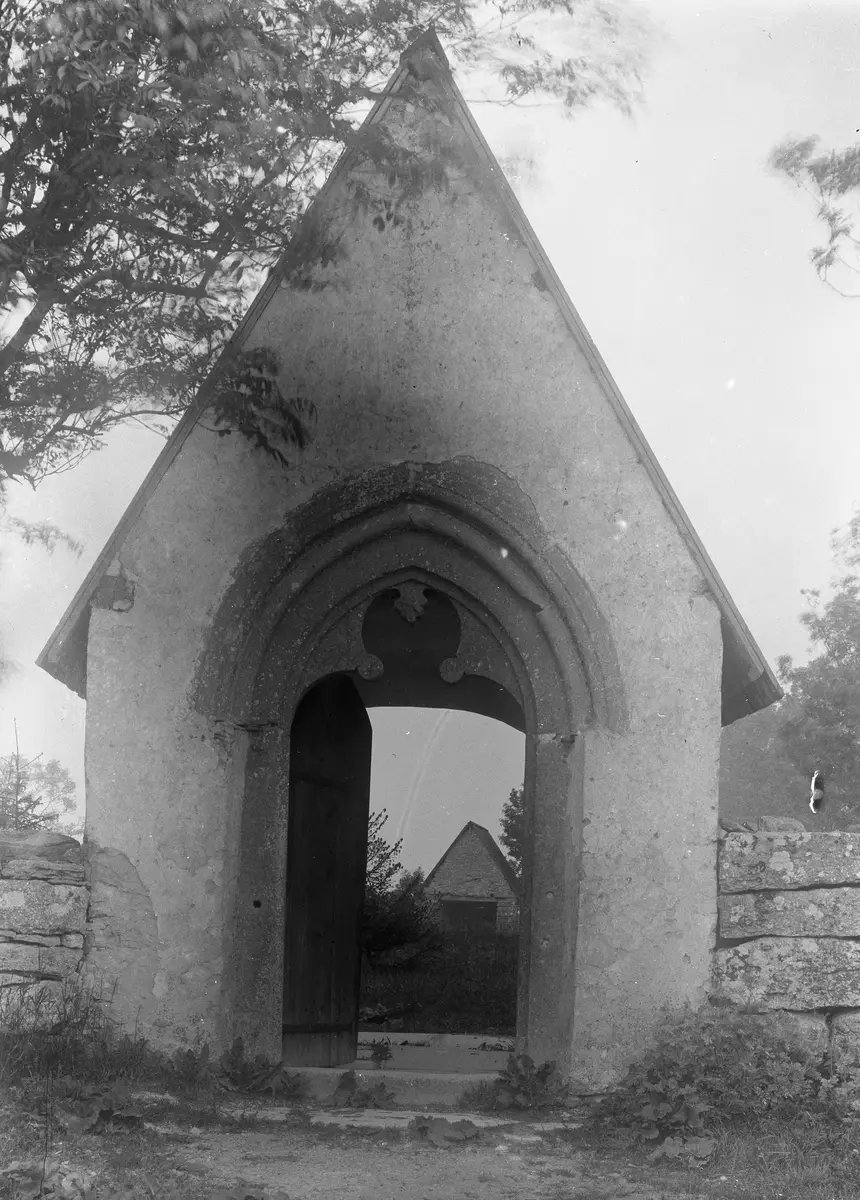 Masse har fotograferat brudluckan från vägen och ställt sig så lågt, att Bönde lucka ses igenom. Brudluckan är ursprunglig från 1200-talet, men återuppbyggd på 1780-talet efter att troligen varit raserad en period. Luckan är byggd i putsad kalksten med fint huggen omfattning med spetsig båge mot vägen. En dörr med omfattning av stående bräder leder besökaren in på kyrkogården. Stigluckan är täckt med ett brant faltak.