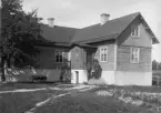 Här ses den år 1910 uppförda nya manbyggnadens baksida, framsidan vetter mot vägen, till skillnad mot den gamla manbyggnaden som hade gaveln mot vägen. Det nya huset är byggt i trä med källare i sten, köks- och kammarbakbygge med vardagsingång och under den nedgång till källaren. Detta måste ha varit en stor investering, vilken man klarade av trots att barnen Oskar och Berta löstes ut med sammanlagt 10 hektar av gårdens omkring 40 hektar jord. Sonen Anton och hans fru Elin övertog gården 1917.

Personerna är troligen fadern Petter Olofsson, 58 år, styvmodern Sofia Katarina, 51 år och sonen Anton Olsson, 30 år.