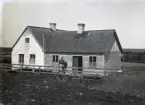 Detta ställe, som en liten gård kallas på Gotland vars avkastning inte är tillräcklig att leva på, bytte ägare omkring 1916, då Lars Östman sålde det till Gottfrid Tingström från Ardre, vars fru kom från Snausarve Södergrens part. Om alla Östmans 10 barn var utflugna när stället såldes är oklart, yngsta barnet var då 15 år. Sonen Emil och hans hustru Emma köpte granngården Gumbalde 1915 och Lars Östman flyttade med dit, kanske också fler ur familjen.

På bilden ser man att den ofärdiga skorstenen på bakbygget från 1912 på Bild 586 är uppbyggd. Kanhända var bakbygget ett bulhus som Östmans flyttade med sig från Snausarve när de byggde här 1877 och att de först bodde i det medan de uppförde stenhuset? Skorstenarna behövde kanske bara lagas, men biten ovanför taket är helt förnyat med silikattegel enligt tidens mode och det är gjort här. Man har tätat vid skorstenarna med plåt. I övrigt ser miljön mycket torftig ut.

Kvinnan på bilden måste vara Gottfrid Tingströms hustru Anny född Hansson från Snausarve, 26 år och deras son med hittills okänt namn som sitter på slantunen.