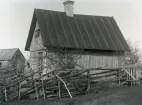 En solig vårdag i maj står Lars Glans, 80 år utanför bostadshuset som sonen Oskar Pettersson flyttat dit 8 år tidigare, se Bild 591. Eller är det Oskar själv, här 47 år? Fruktträden har ännu inte slagit ut, men de är så stora, att det knappast är tänkbart att skulle vara planterade för 8 år sedan, se Bild 595.

Oskar var klockare och brevbärare från 1889 ända till sin död 1933, han gick med posten mellan Lau och När. Oskar var gift med Svea född Jakobsson från Stockholm. Hon var 20 år yngre än Oskar och övertog postjobbet efter honom, som hon hade till 1950. Då blev Lau egen poststation för en tid, vars föreståndare blev dottern Ingrid, som hade postexpedition hemma i det tidigare tillbyggda bostadshuset. Boplatsen och huset finns alltjämt kvar.

I bildens bakgund ses uthusen, så man får en uppfattning om hur de står i förhållande till varandra. Det innebär att uthusen stod alldeles ute vid stora vägen, ungefär där infarten till Lau f d kvarn går idag.