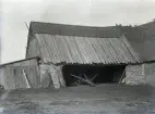 Här ses gårdens tröskhus med fal- och spåntak. Man kan se att faltaket är lagt med bredare underfalar och smalare överfalar. De är inte längdjusterade efter påläggningen, det brydde man sig ofta inte om på uthus, utan falarna fick ha den längd de fick vid apteringen i skogen, nästan alltid 7 alnar, dvs 4.20 m. De korta falarna upptill har blivit dåliga och då har man spikat på ett spånskikt över dem. Vandringshjulet finns ännu kvar. Skjulet på gaveln är nog inte så gammalt, trots att det lutar. Grenhopen mot tröskhuspelaren skyddas delvis av en avbruten kvarnvinge.