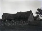 Gaveln och baksidan av fähuset är helt slutna, det ser inte ut som om det ens finns gödselluckor. Det branta agtaket börjar bli dåligt. Den obligatoriska stegen hänger under takskägget. Även tröskhusets tak har börjat sjunka ihop litet. Ladugården i bakgrunden har genomgått en modernisering.