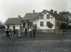 Larssons har utökat huset med ett köksbakbygge och byggt ihop det med flygeln och här har man fått en vardagsingång via en liten farstukvist.

Masse har ställt upp delar av familjen framför huset. Från vänster ses troligen mågen Jakob Larsson 27 år, hustrun Elisabet 51 år med hund, okänd, Oskar 57 år, dottern Emilie 27 år och okänd. Möjligen är de okända Masse själv med hustrun Majken.