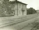 Birger Sjöströms hem, SJ.s tjänstebostad, Stationsgatan, kvarteret Köpmannen, Hudiksvall. Huset har stora fönster och en balkong ut mot järnvägsspåren. Till vänster syns ett stort träd samt stege som står lutad mot husets tak. Ett staket omgärdar huset.