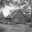 Södra Arlebrunn i Vånga socken, nära och historiskt tillhörigt egendomen Grensholm. Enkelstugans okonventionella yttre får tillskrivas godsets traditionsfrihet och specifika materialtillgång som alltemellan kom i uttryck i herrgårdars tjänstebostäder.