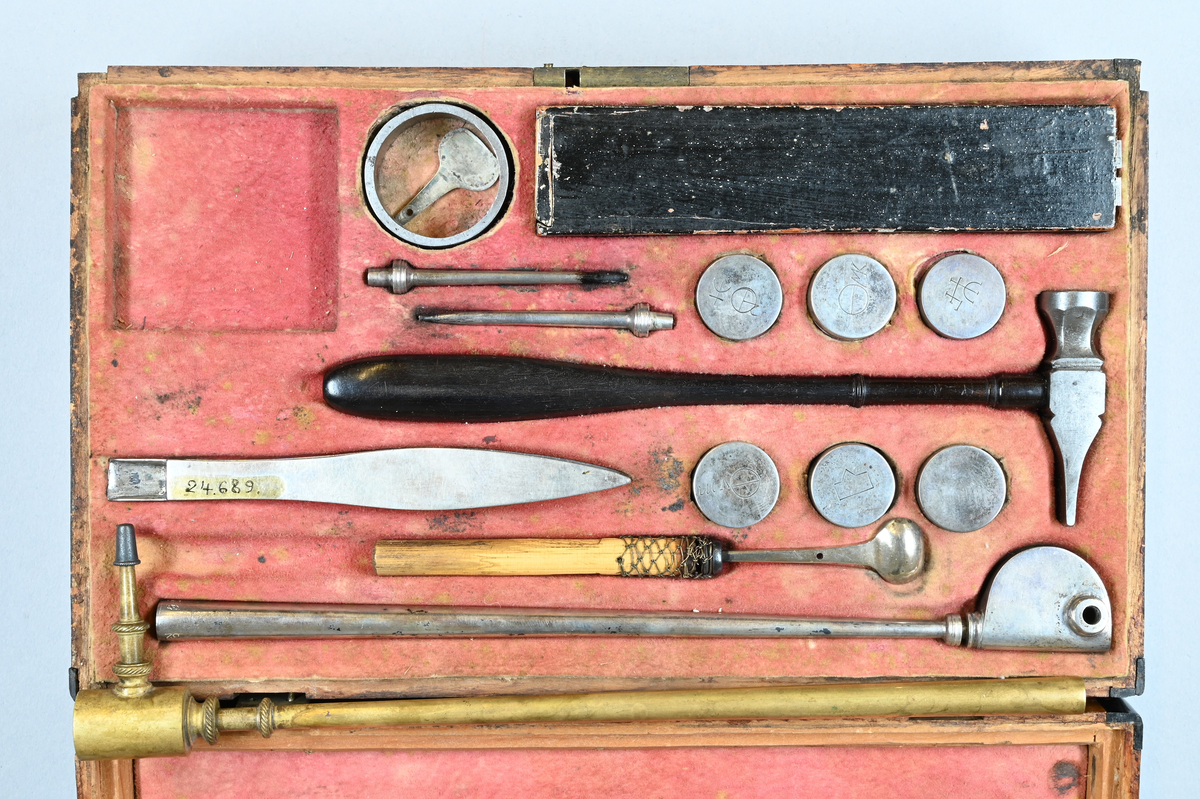 Reagensbestick för blåsrörsanalys, i fodral av trä. Lösa delar: isärtagbart blåsrör av silver, troligen av Bergmans typ, två blåsrörsmunstycken av silver, liten degel av silver med vridbart lock och skaft av trä, hammare med skaft av ebenholts, ring av stål till kross, sex reagensdosor av silver, med lösa lock med kemiska tecken, enligt Scheffer-Bergman jämte reagens (kalkspat, gips, borax (?), salpeter (?), alkalisalt), pincett av silver med "kattfot" och "B 2" END B=S:t Erik? (=1784), två stavmagneter med två armeringsjärn och trästav i fodral av papp och trä, fodral, skjutlåda, blåsrör av mässing av Berzelius typ. Kvadratisk stöd av stål och nyckel till fodralet och skjutlådan saknas. Måtten avser fodralet.