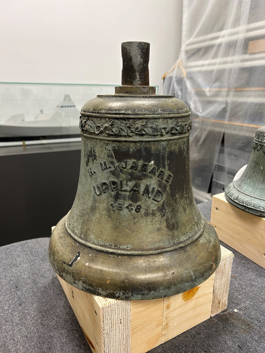 Skeppsklocka av brons märkt i relief: "HM Jagare Uppland 1948". Ornamentslinga vid vid klockans topp. Kläpp av stål.