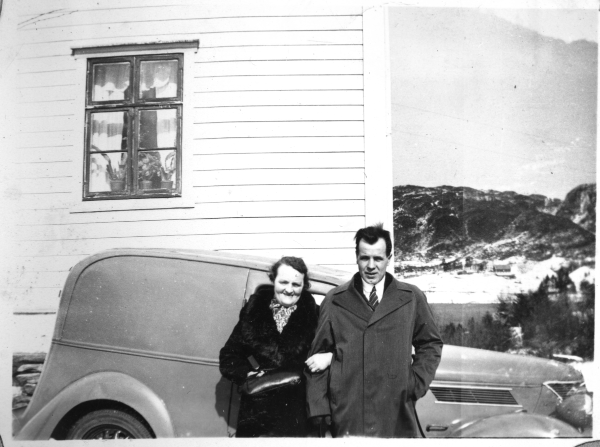 Ei kvinne og ein mann som står framfor ein bil som er parkert ved eit bustadhus.