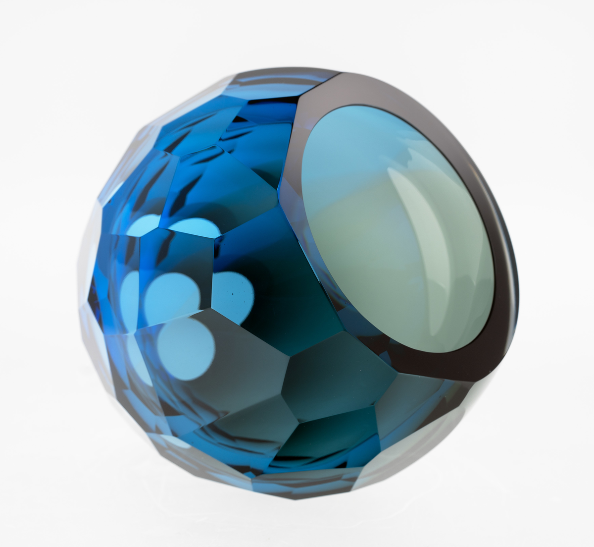 Ovalformet skulptur i farget gjennomskinnelig glass. Yttersiden er fasettert ved hjelp av sliping og har sirkulære åpninger på hver av kortsidene. Massen graderes fra grå mot blå, og overflaten veksler mellom mørke og lysere partier.