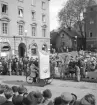 Arrangemang i Linköping 1944 genom ett ögonblick från Stora torget. I stunden passerar ett ekipage med reklam för Björklunds speceri.