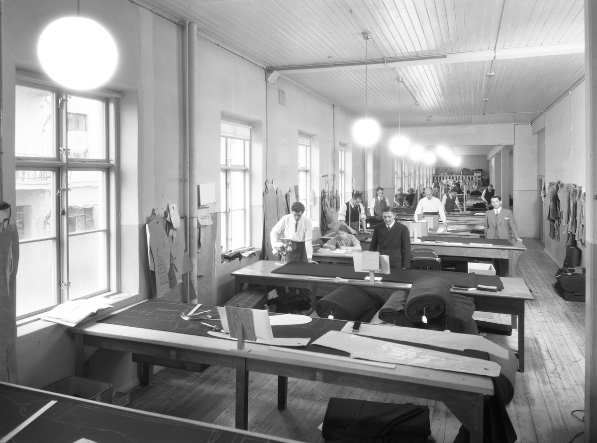 A-B. Bergsson och söner; interiör av fabriken. Tillskärare i arbete.
Företaget som var känt över hela vårt land som ett av de större i konfektionsbranschen och grundades 1900 av framlidne grosshandlaren B.Bergsson och hans två äldsta söner som grosshandelsfirma i manufakturbranschen. 1914 upptogs egen tillverkning av herrkläder. 1929 skedde en första tillbyggand av fabrikslokalerna. Åren 1935-36 utökades fabrikslokalerna till det dubbla och företaget har kunnat glädja sig åt ett fullt utnyttjande av sin kapacitet c:a 40.000 plagg per år. Firman hade även upptagit tillverkning av damkappor och damdräkter.
Källa: Nyblom-Svanqvist, Näringsliv i Värmland.1945.