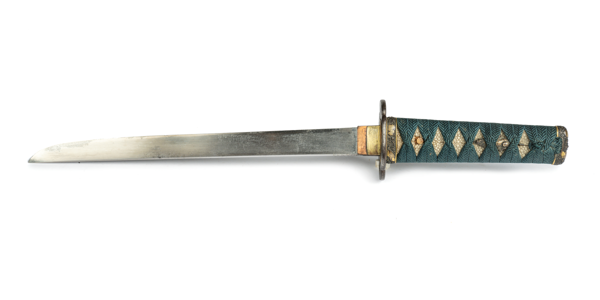 Samurai-dolk (WAKICACHI) från Japan. Klinga svagt bakåtböjd,eneggad, skarp, facetterad rygg. Fäste av vitt hajskinn flätat med grönt bomullsband med två amuletter, delvis förgyllda. Beslag upptill och nedtill cicilerade och förgyllda. Parerplåt rund med ett hål på ena sidan samt med förgyllt och cicilerat bladverk. Balja av trä, svartlackerad med beslag å fyra ställen.
Låsfjädern,d.v.s. bestickknivens handtag saknas.
Kniven på baljan (KOZUKA) saknas.
Från fregatten VANADIS världsomsegling 1883-85.