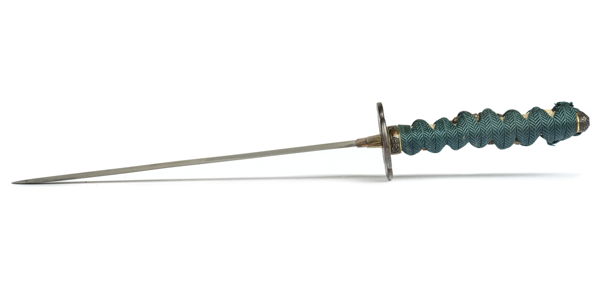 Samurai-dolk (WAKICACHI) från Japan. Klinga svagt bakåtböjd,eneggad, skarp, facetterad rygg. Fäste av vitt hajskinn flätat med grönt bomullsband med två amuletter, delvis förgyllda. Beslag upptill och nedtill cicilerade och förgyllda. Parerplåt rund med ett hål på ena sidan samt med förgyllt och cicilerat bladverk. Balja av trä, svartlackerad med beslag å fyra ställen.
Låsfjädern,d.v.s. bestickknivens handtag saknas.
Kniven på baljan (KOZUKA) saknas.
Från fregatten VANADIS världsomsegling 1883-85.