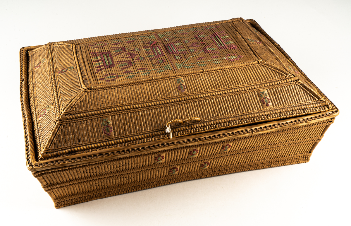 Hårt flätad korg i spån med inbroderat mönster i rött och grönt på lock och sidor.