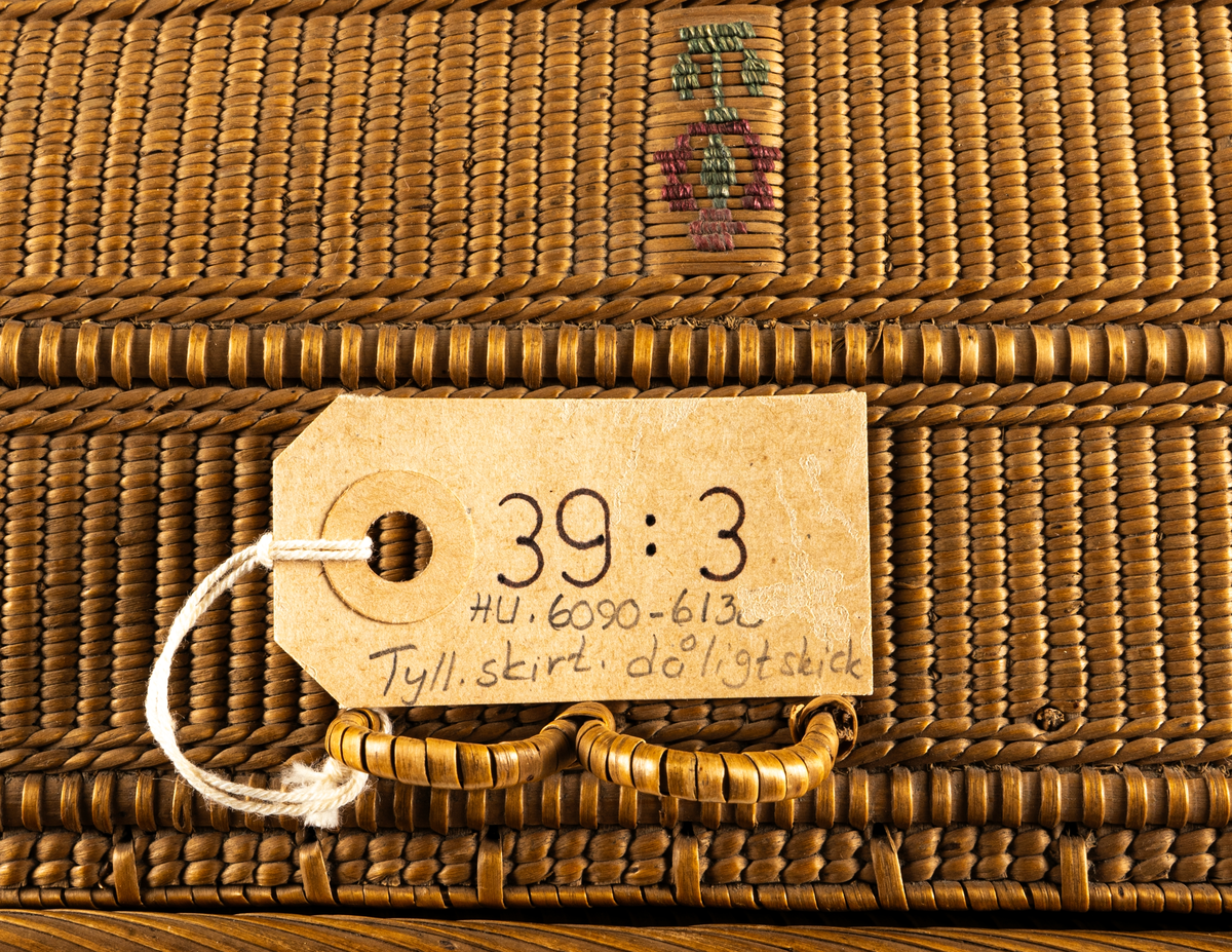 Hårt flätad korg i spån med inbroderat mönster i rött och grönt på lock och sidor.