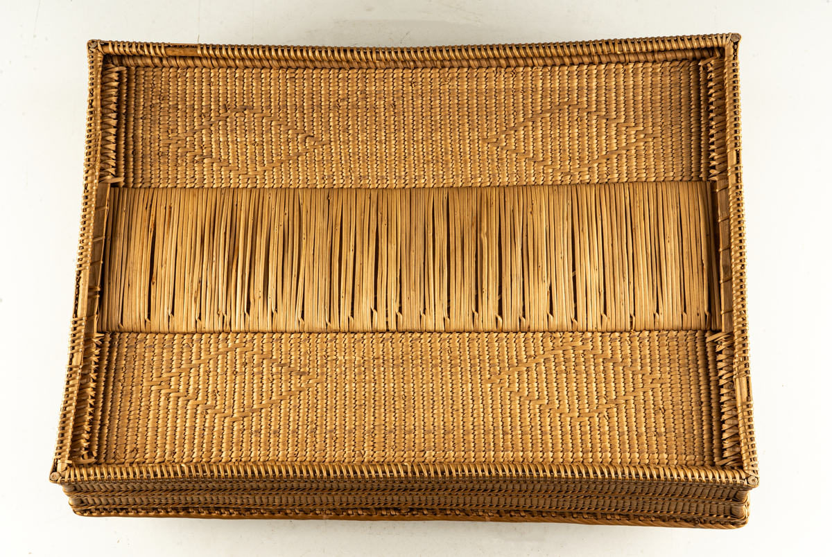 Hårt flätad korg i spån med inbroderat mönster i rött och grönt på lock och sidor.