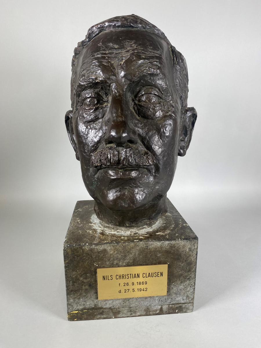 Bronsebyste av Nils Christian Clausen (1869-1942). Festet med en lang skrue til en sokkel av stein med navneplate.