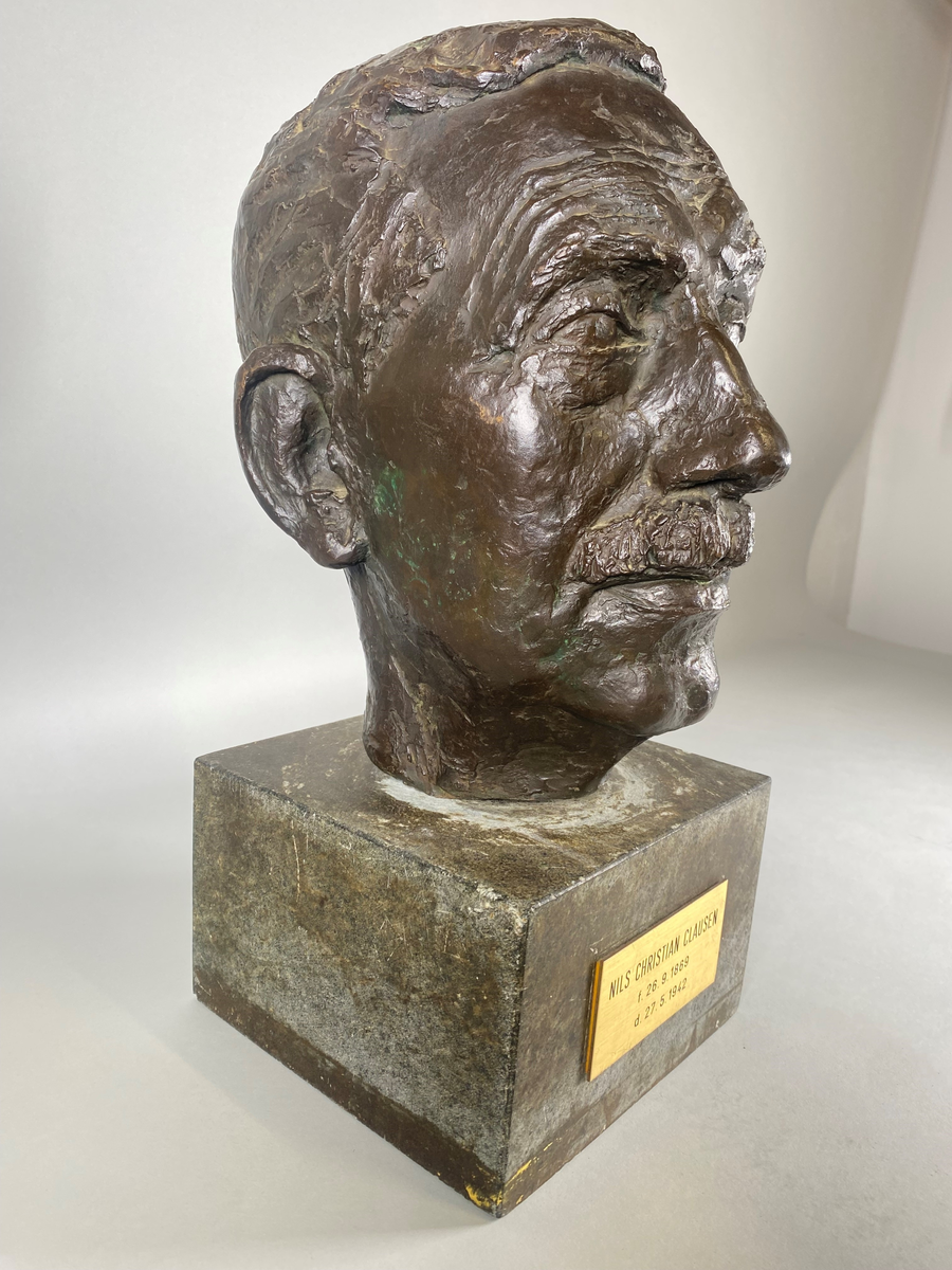 Bronsebyste av Nils Christian Clausen (1869-1942). Festet med en lang skrue til en sokkel av stein med navneplate.