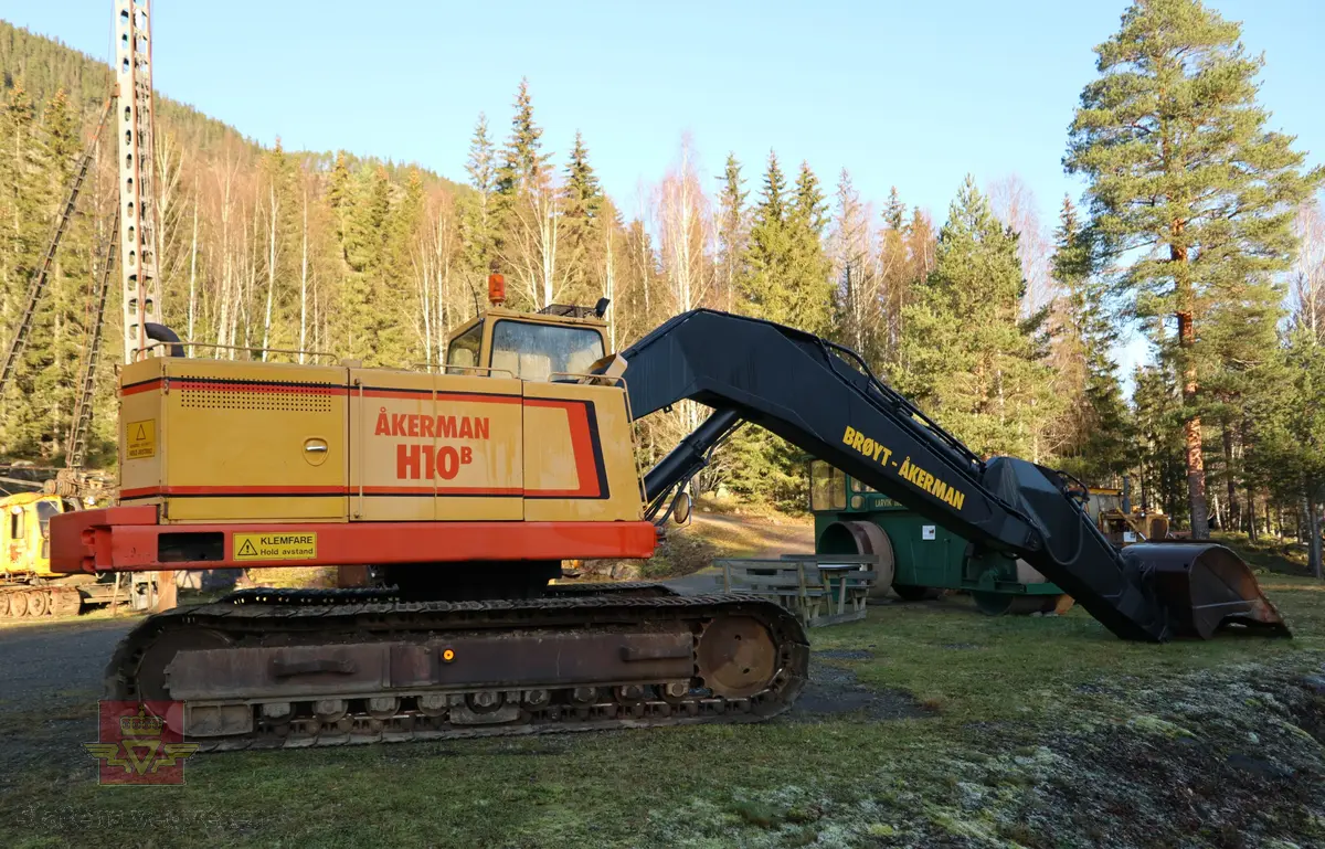 Åkerman H10B gravemaskin. Beltegående. Gul, rød, og svart. Merking fra produsent og første bruker. Maskina har en dieseldrevet Volvo Penta TD61ACE motor, den yter 166 Hk (122 kW). Motoren er 6-sylindret, 4-takt, med vannavkjøling, direkte innsprøytning og turbo. Det elektriske systemet er 24V. Drivstofftanken rommer 340 liter. Lydnivået er 77dB (målt 10 meter fra maskinen). Serienummer er 2632.
Maskinen har gått 10.000 arbeidstimer.