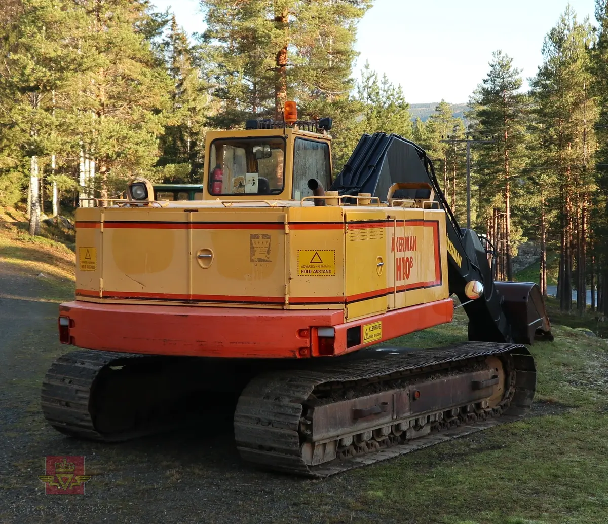 Åkerman H10B gravemaskin. Beltegående. Gul, rød, og svart. Merking fra produsent og første bruker. Maskina har en dieseldrevet Volvo Penta TD61ACE motor, den yter 166 Hk (122 kW). Motoren er 6-sylindret, 4-takt, med vannavkjøling, direkte innsprøytning og turbo. Det elektriske systemet er 24V. Drivstofftanken rommer 340 liter. Lydnivået er 77dB (målt 10 meter fra maskinen). Serienummer er 2632.
Maskinen har gått 10.000 arbeidstimer.