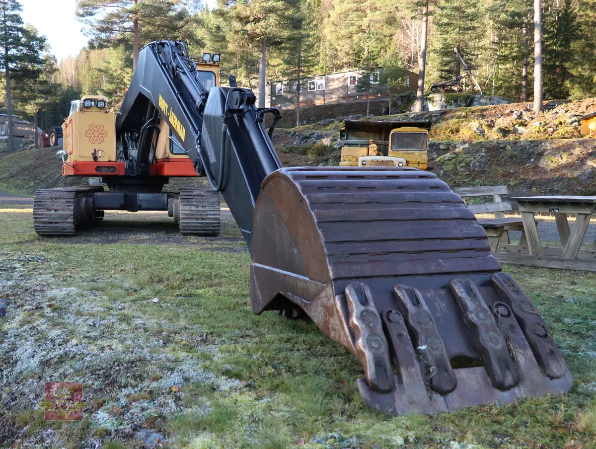 Åkerman H10B gravemaskin. Beltegående. Gul, rød, og svart. Merking fra produsent og første bruker. Maskina har en dieseldrevet Volvo Penta TD61ACE motor, den yter 166 Hk (122 kW). Motoren er 6-sylindret, 4-takt, med vannavkjøling, direkte innsprøytning og turbo. Det elektriske systemet er 24V. Drivstofftanken rommer 340 liter. Lydnivået er 77dB (målt 10 meter fra maskinen). Serienummer er 2632.
Maskinen har gått 10.000 arbeidstimer.
