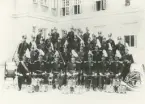 Gruppbild av militärmusikkår med sina instrument utanför en kanslihusbyggnad.