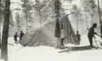 Fyra soldater i en snöklädd skog ordnar med ett stort tält.